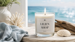 LILIEN Duftkerze aus Sojawachs mit personalisiertem Etikett in maritimer Umgebung mit Muschel, Treibholz und Meer im Hintergrund.