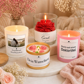 Vier personalisierte LILIEN Kerzen in einer warmen, gemütlichen Produktszene: eine Fotokerze im Milchglas, eine rote Rosenkerze im Glas mit „Happy Birthday Sarah“, eine rosa Kerze mit dem Spruch „Riecht nach einem Doktortitel“ und eine goldene Wunschtext-Kerze mit rosa Blüten, dekoriert mit Trockenblumen auf hellem Stoff.